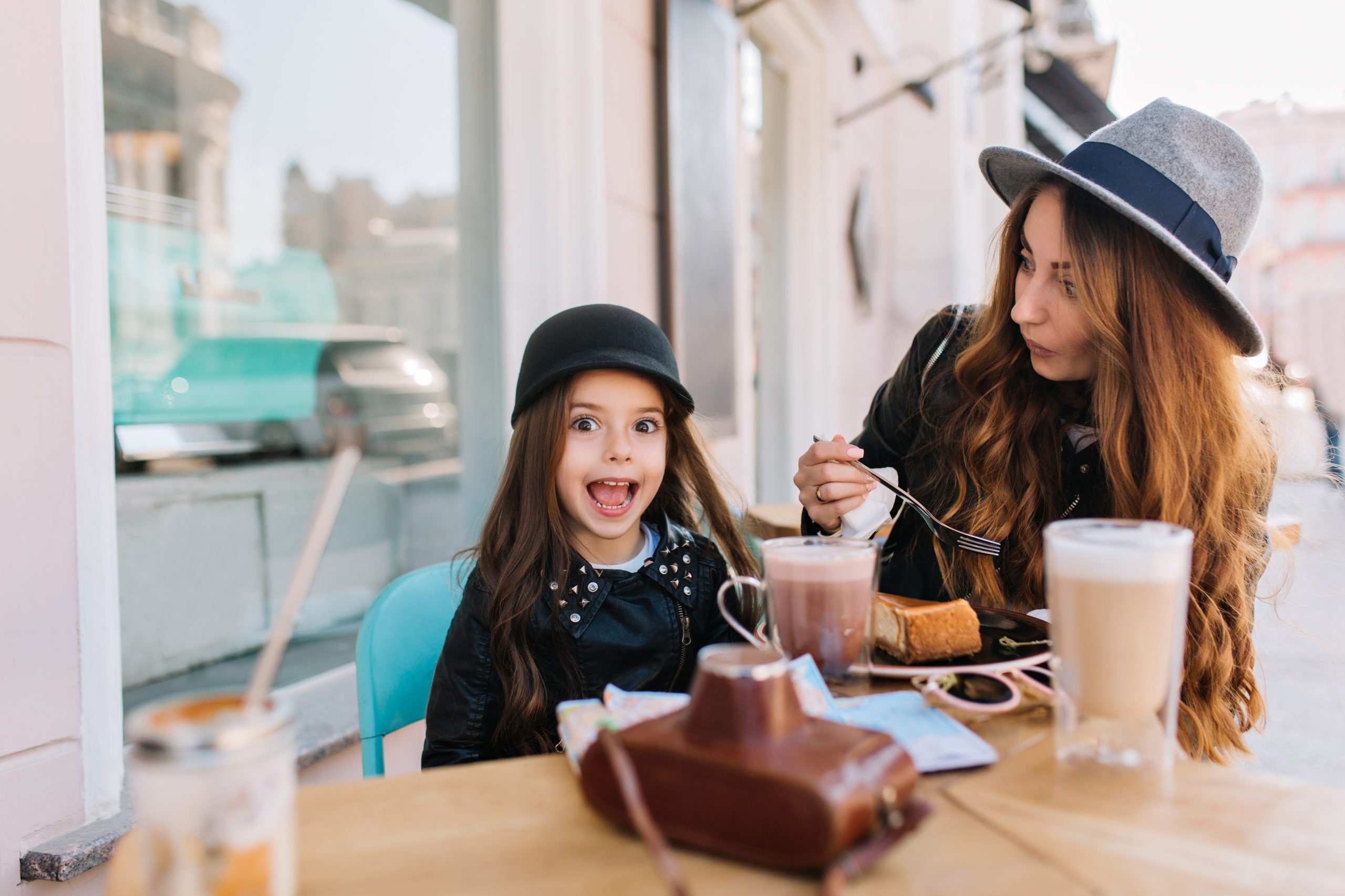 Amazing young woman in vintage gray hat eating tasty cheesecake with her little sister in weekend. S